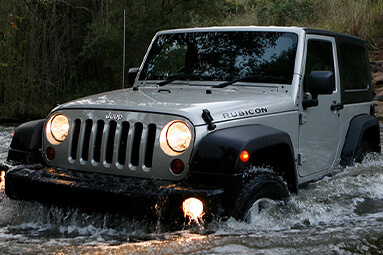 Black Jeep Wrangler in forest driving through river 
