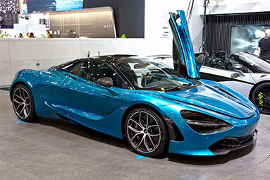 Front side view of a blue McLaren with the left front door open in a showroom.