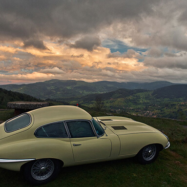 Classic cream Jaguar parked on a hilltop overlooking green fields