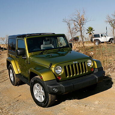 Green Jeep Wrangler driving on dirt path safari with other Jeeps in background