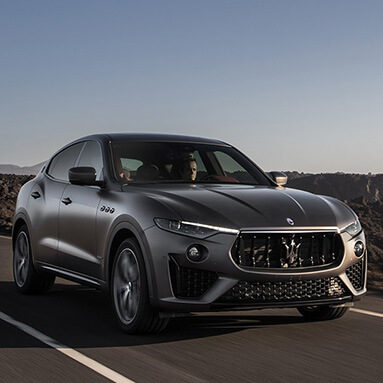 Silver Maserati Levante Vulcano being driven by a man with mountains in side view and sun shining into car.
