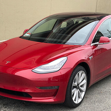 Front side view of a maroon Tesla Model 3.