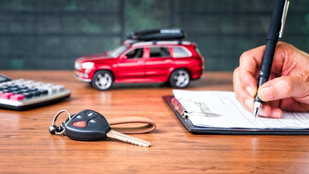Car keys and calculator on a desk next to a person signing a Car Insurance contract, symbolising savings from comparing premiums online.