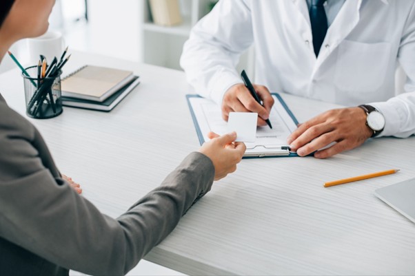 Patient handing a card to a doctor who is writing on a clipboard, representing a medical consultation and choosing Gap Cover to fund healthcare shortfalls.