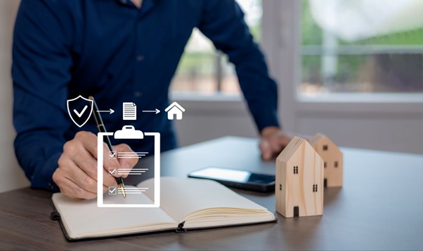 Person writing in a notebook with wooden house models and digital insurance icons, representing planning and comparing Home Contents Insurance cover.