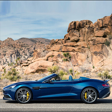 Side view of the cobalt blue 2014 Aston Martin Vanquish Volante with rocky mountain background.