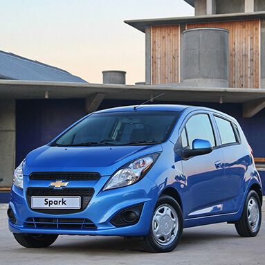 Side front view of a blue Chevrolet Spark in front of a building.