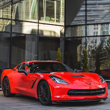 Front side view of the red Chevrolet Corvette in front of building with glass panels. 
