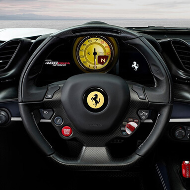 Inside view of ferrari with branded, black steering wheel, push to start button and gauge.