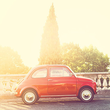 Red classic Fiat, parked side view shot with a golden sunny glow.