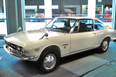 White Isuzu 117 Coupe 001 parked in showroom.