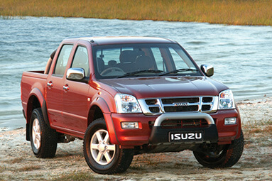 Maroon isuzu bakkie parked on sandy ground with river behind it.