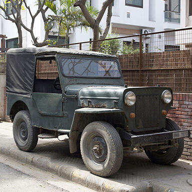 Classic military green, muddy jeep parked on the pavement, outside a house.