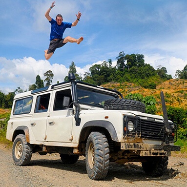 Smiling man jumping over white Jeep with mountain and blue sky back ground