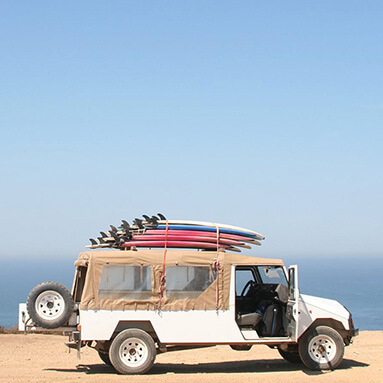 White Jeep parked sideways with blue skies and beach in the background