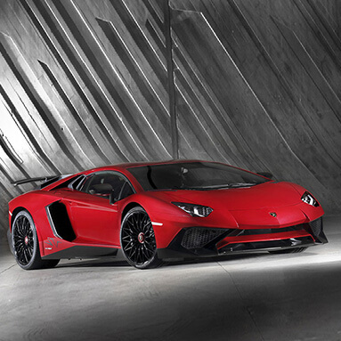 Red lamborghini aventador, parked indoors with grey wall behind.