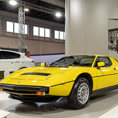 Yellow maserati on top of platform in a white warehouse.