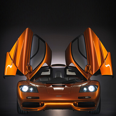 Front view of the McLaren F1 with both doors open and head lights on.