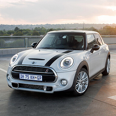 White MINI Cooper S 5-Door with two black stripes in front on rooftop with green vegetation.