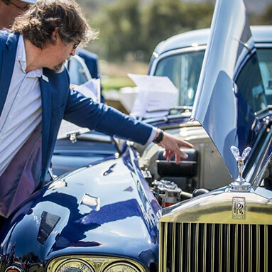 Man pointing inside the open hood of a Rolls-Royce classic