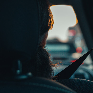 Woman sitting in a car with seatbelt on staring at a sunset.