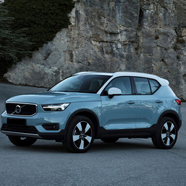 Grey Volvo parked sideways on tar road, in front of mountain rock face.