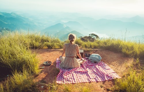 Woman wearing a grey sleeveless dress, sitting on a mountain