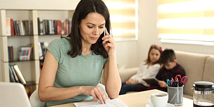 Woman on phone working at a desk with kids in the background.