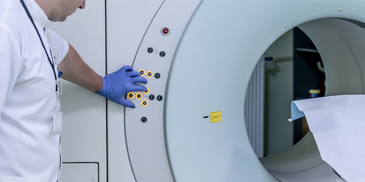 Man wearing white lab coat and medical gloves switching on MRI scanner.