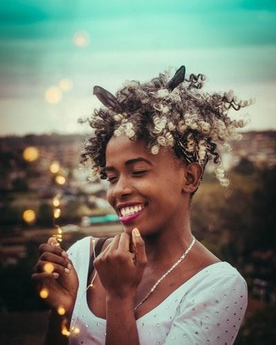 Young lady laughing and smiling, holding Christmas lights with eyes closed.