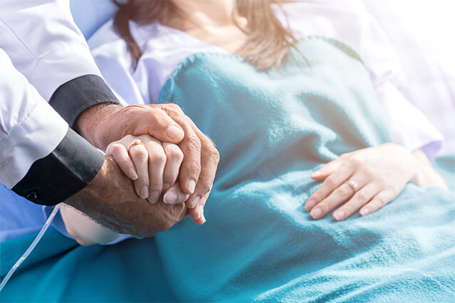 Lady in hospital bed, doctor holding her hands