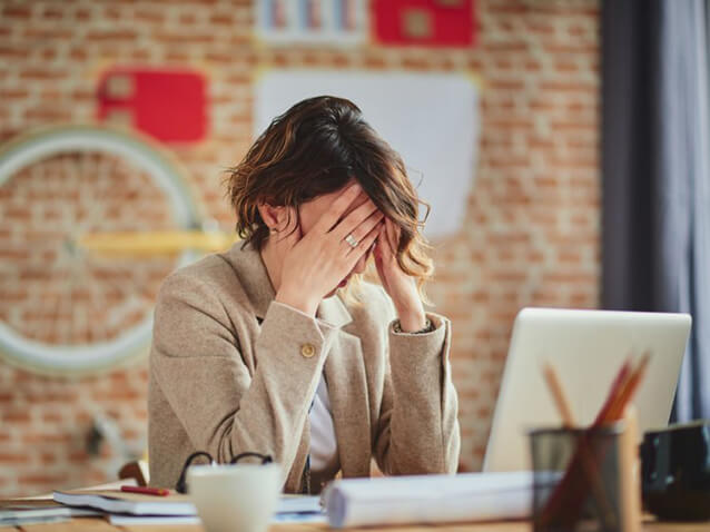 Woman sitting at a desk holding her face with both hands