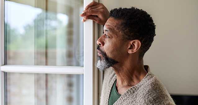 Man staring out of window thinking of how COVID-19 increases risk to other medical conditions