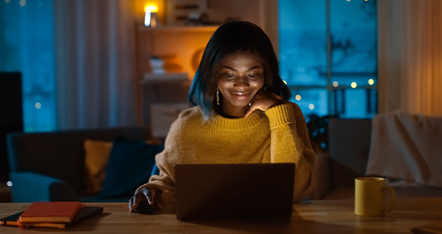 A woman looking at her laptop in the evening sat at a table