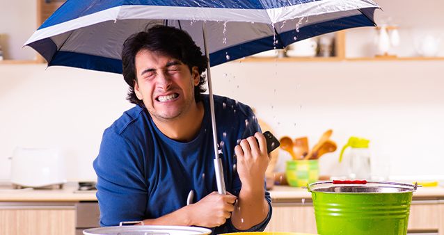 A man sheltering from rain under an umbrella in is kitchen