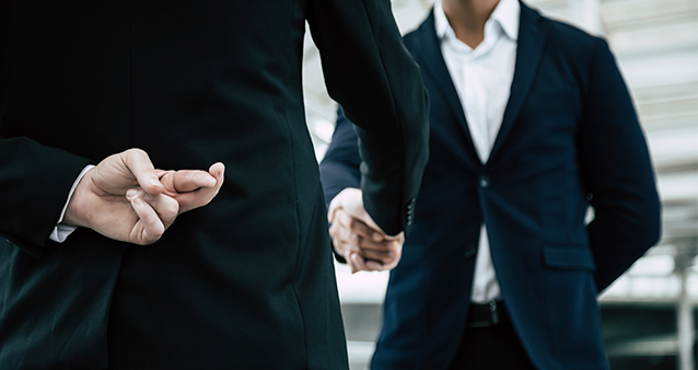 man crossing fingers behind his back while shaking hands