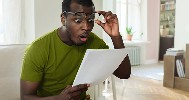 shocked young man looking down on papers in hand lifting his spectacles from his eyes