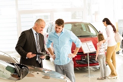 Sales manager/agent assisting a male customer while women and girl looks at a red car