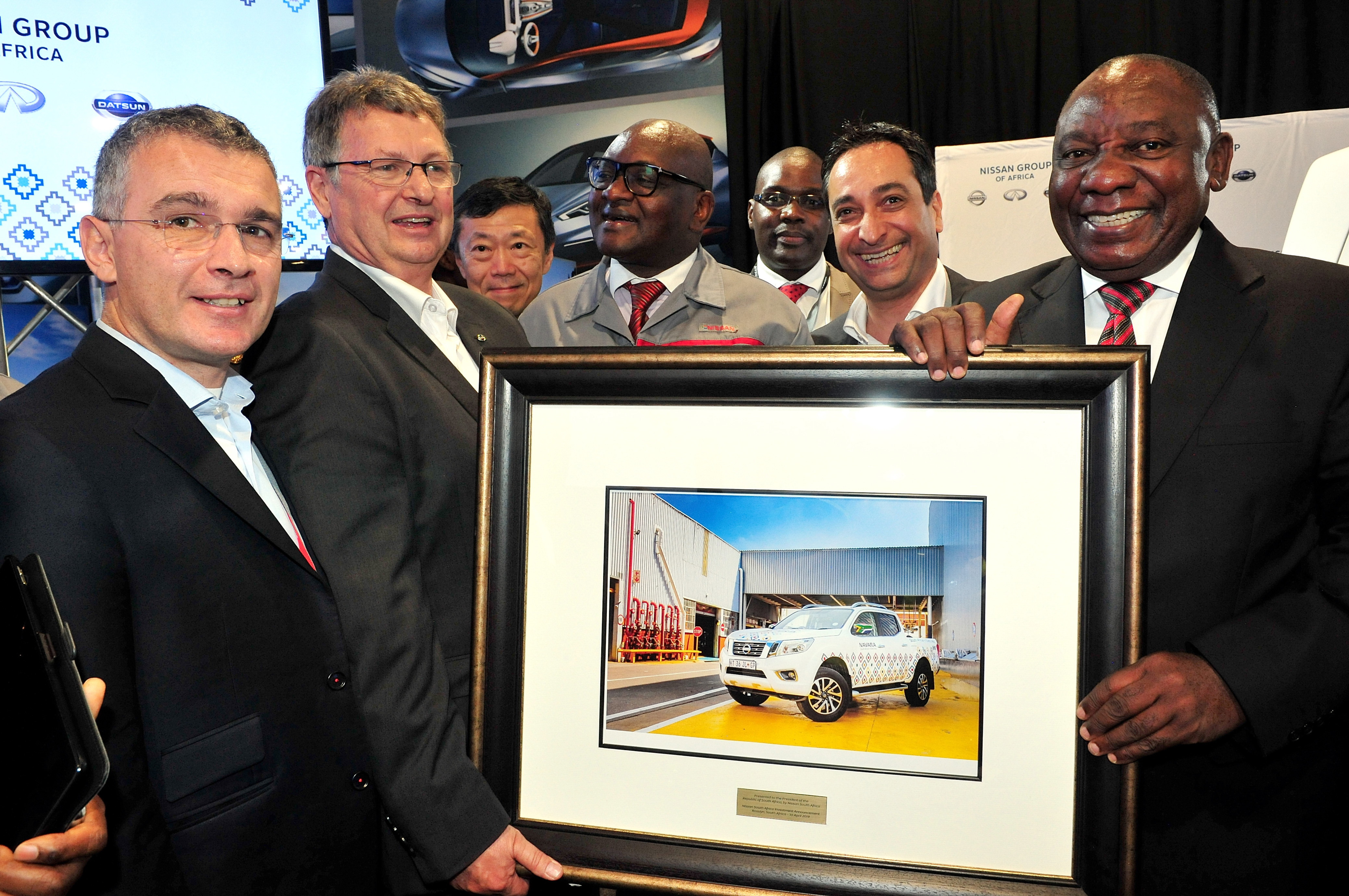 South African President Cyril Ramaphosa with Nissan delegates, holding a framed picture of a Nissan Navara. 