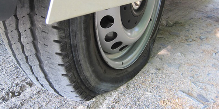 Flat and damaged car tyre parked on a rough floor.