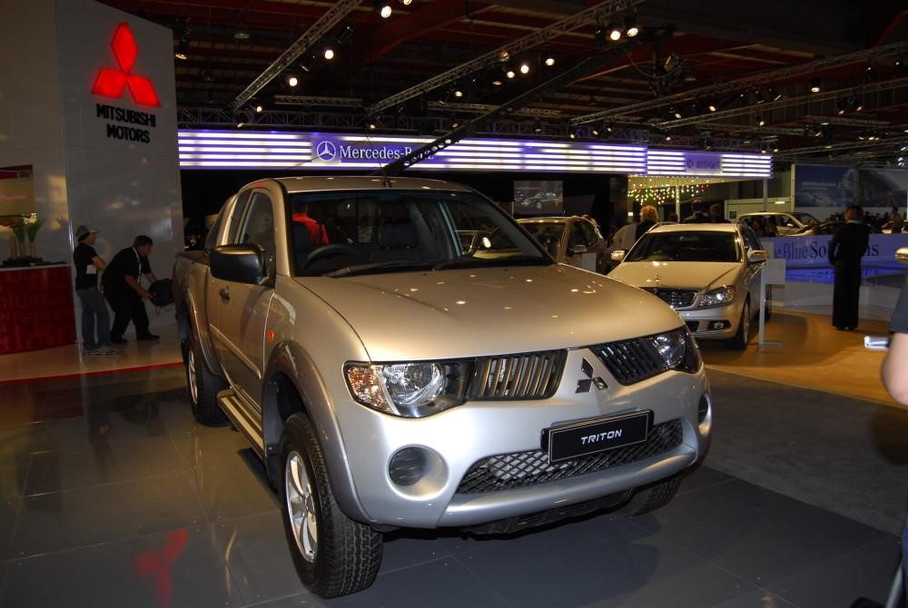 Silver Mitsubishi Triton parked on display with sales people in background.
