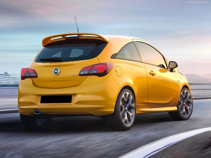 Moving yellow Opel Corsa, rear view image with blue skies.