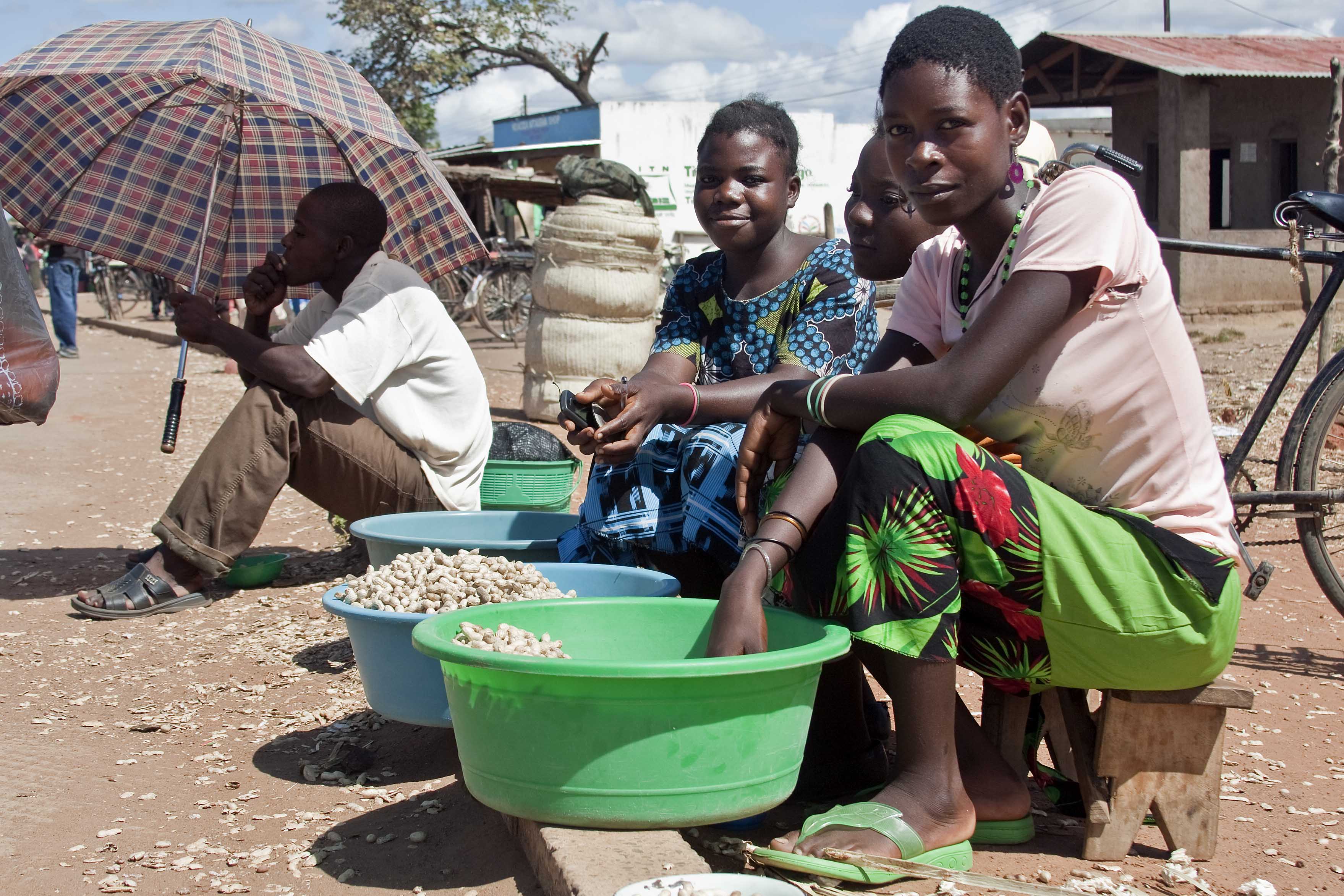 Young women sitting on benches selling nuts out of basins.