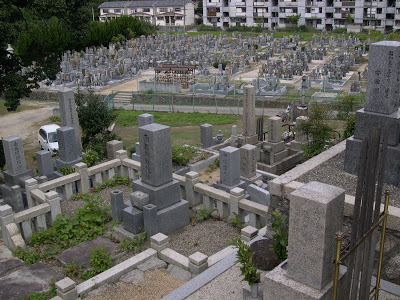 Modern day Japanese graveyard with tombstones and buildings in the background.