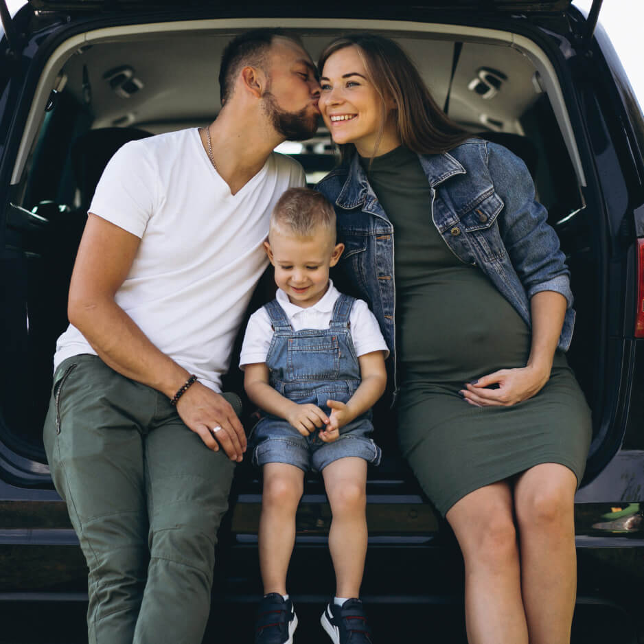 Young family with son and pregnant mom sitting in the boot holding each other