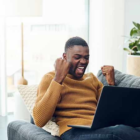 Excited young man on couch looking at computer