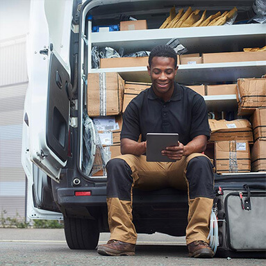 Man with ipad in hand sitting in van with the doors open revealing all the parcels 