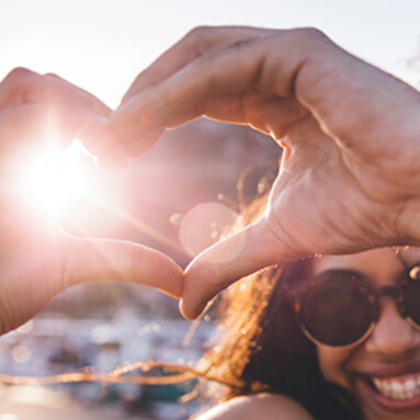 Lady with hands in shape of heart with sun shining in background