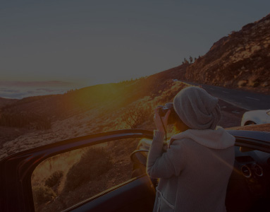 Lady standing with passenger car door open taking pictures of the sunset | History of Rentalcars.com | hippo.co.za partner