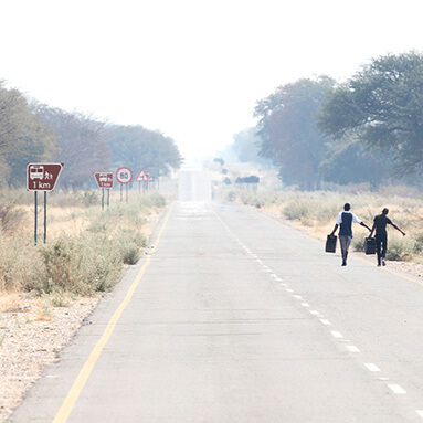 Long stretch of tar road with children walking in street carrying items.